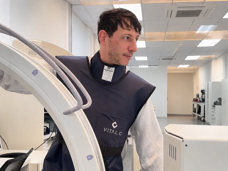 Técnico da Vital C com avental de proteção ao lado de um arco cirúrgico no laboratório