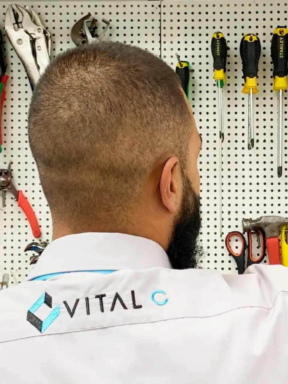 Técnico da Vital C, de costas, diante da parede de ferramentas do laboratório