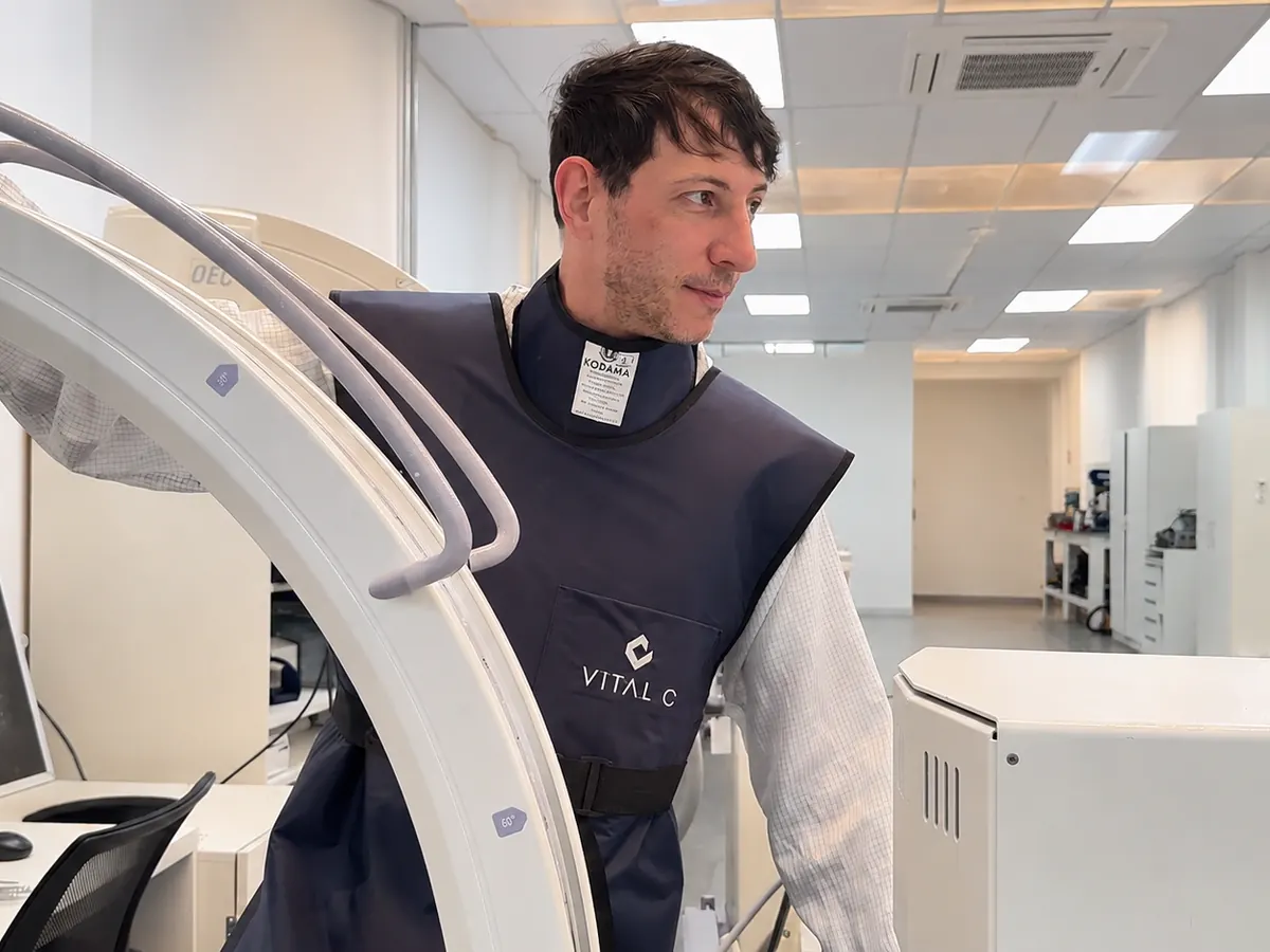 Técnico da Vital C com avental de proteção ao lado de um arco cirúrgico no laboratório